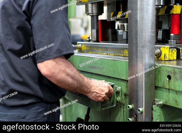 Steel Manufacturing Plant. A Worker is Placing a Piece of Metal Inside the Press. The Press is pushed Down. Metallurgy. Production Process. Close up
