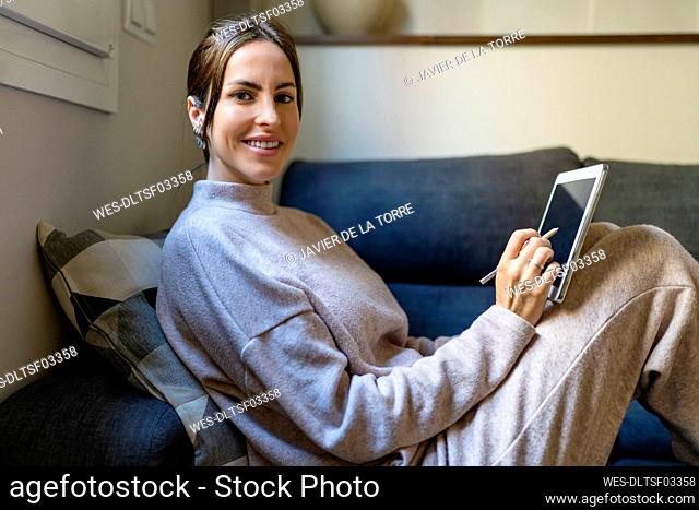 Happy young woman with table PC sitting on couch at home