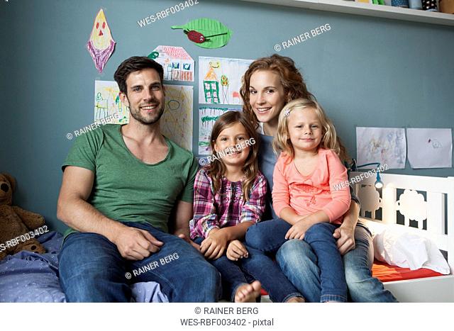 Family picture of couple with her little daughters sitting together on bed in children's room