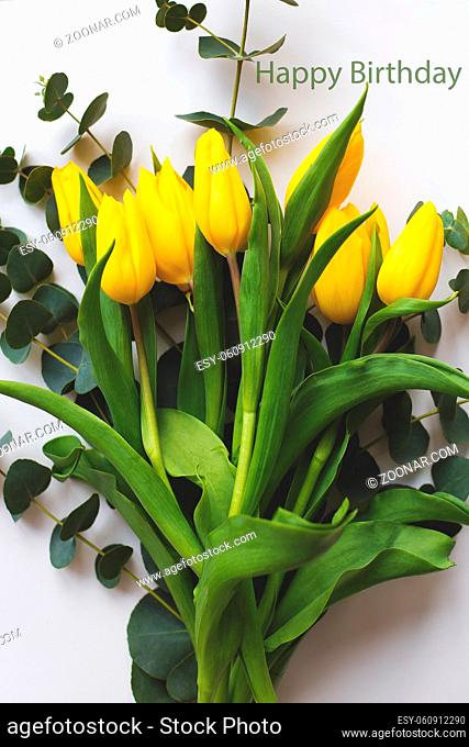 Beautiful yellow tulips on a white table, inscription happy birthday