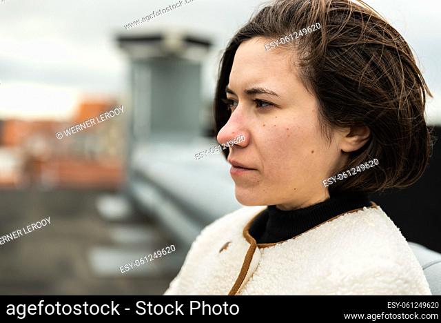 Outdoors portrait of a 28 year old white woman with wind in her brown hair, sitting on a rooftop. , Brussels, Belgium