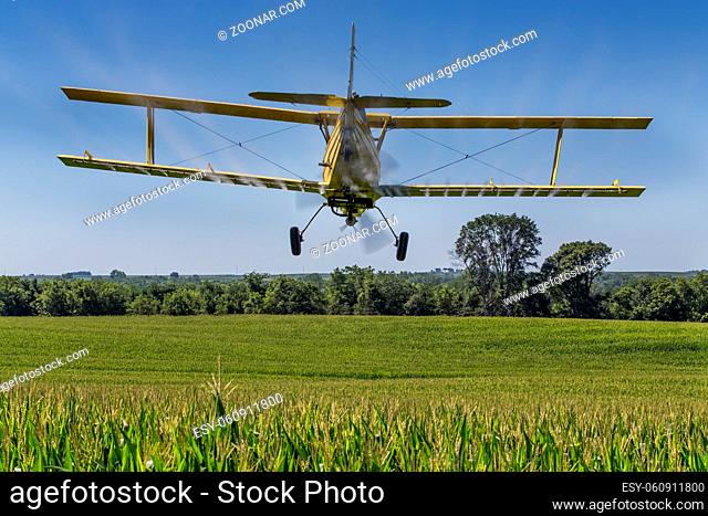 A crop duster applies chemicals to a field of vegetation