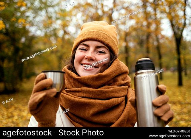 Smiling young woman with insulated drink container at autumn park