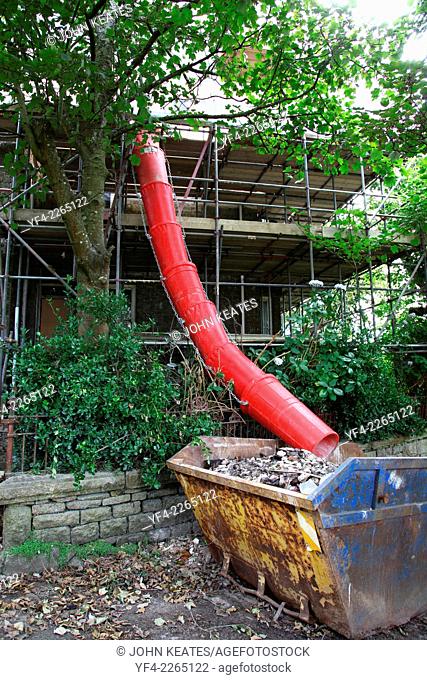A red builders chute channelling rubble into a skip St. Just, Cornwall, England, UK