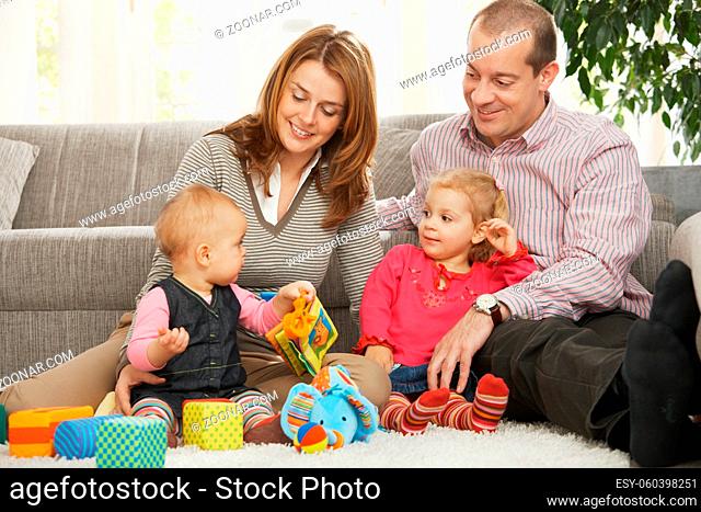 Smiling parents and small daughter looking at baby sitting on floor