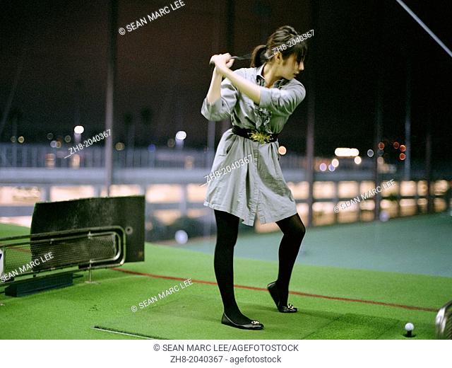 A young woman in a dress playing golf at a driving range in Korea Town, Los Angeles