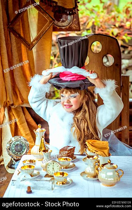 An little beautiful girl in the scenery of Alice in Wonderland holding cylinder hat with ears like a rabbit over head at the table in the garden