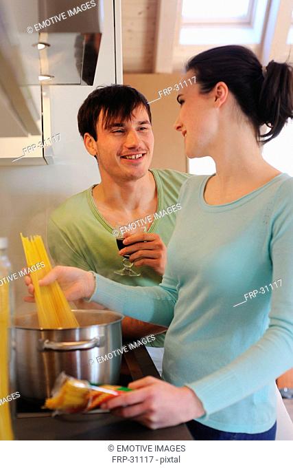 Young couple in kitchen cooking spaghetti and drinking red wine