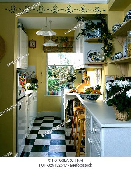 Black and white vinyl floor tiles in yellow galley kitchen with stencilling above doorway