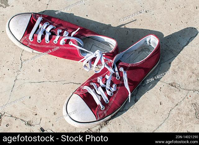 Pair of worn out vintage red old canvas sneakers on outside concrete surface