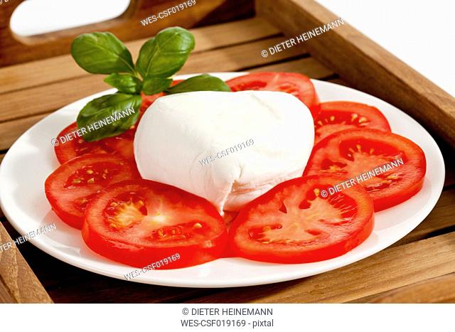 Buffalo mozzarella with basil and tomatoes on plate, close up
