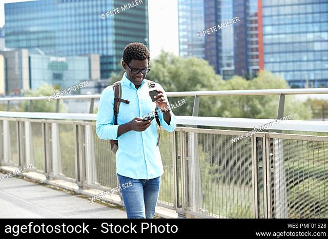 Man using smart phone while holding disposable coffee cup walking on footpath in city