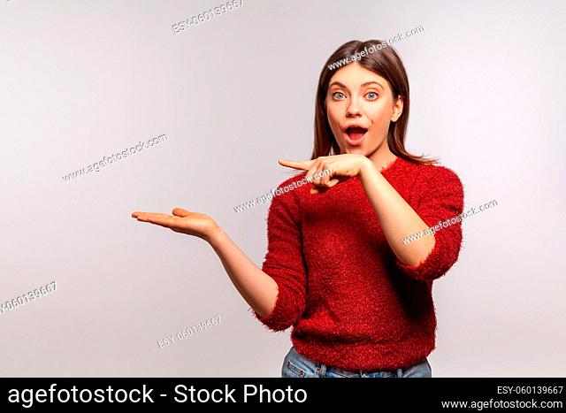 Wow, attention at advertisement. Portrait of surprised shocked girl pointing at empty space on her palm, blank wall for commercial idea, product image