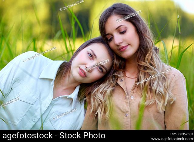 Two young women brunette and blonde are standing in a field. Romantic female couple in tall grass. One girl put her head on her friend's shoulder