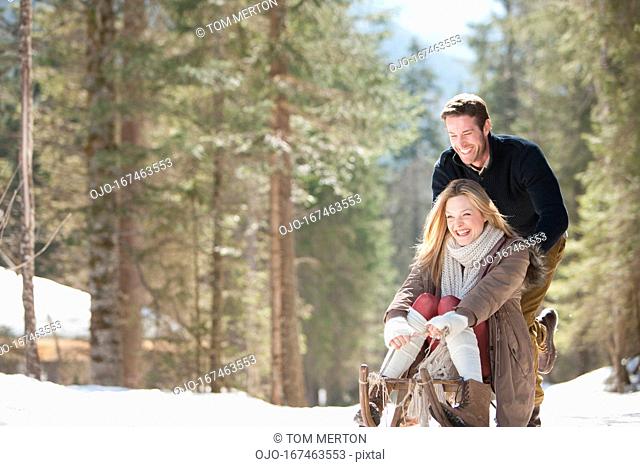 Man pushing woman on sled in snowy woods