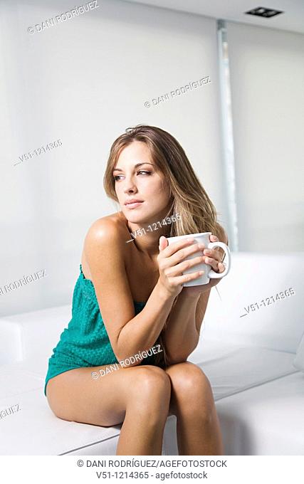 Blonde spanish woman sitting in a sofa at home with a drink and thinking