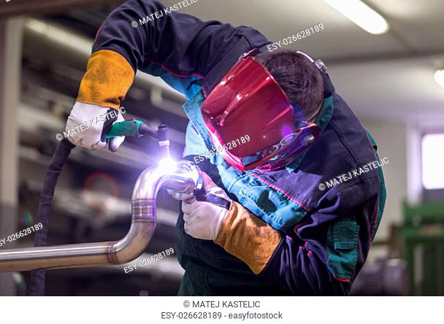 Industrial worker with protective mask welding inox elements in steel structures manufacture workshop