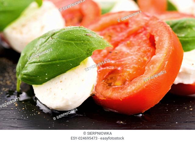 Caprese salad with mozzarella, tomato, basil and balsamic vinegar arranged on black plate