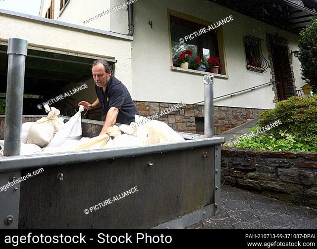 13 July 2021, Rhineland-Palatinate, Mayen: Resident Rolf Schneider unloads sandbags in front of his house. Heavy rain is forecast for parts of the Eifel