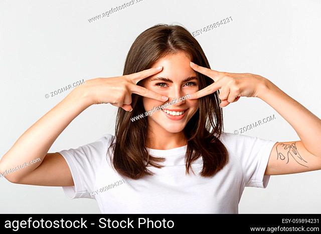 Close-up of sassy attractive brunette girl showing peace gestures over eyes and smiling happy