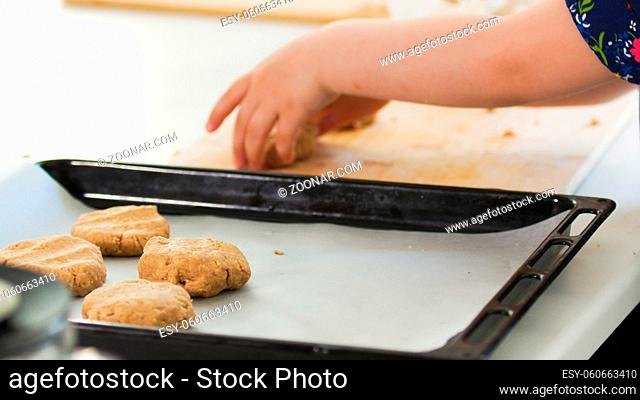 Preschool girl baker puts homemade cookies on a baking sheet, close up