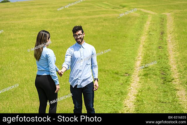 Two smiling lovers in the field holding hands, Beautiful couple holding hands looking at each other in the field, two persons holding hands in the field