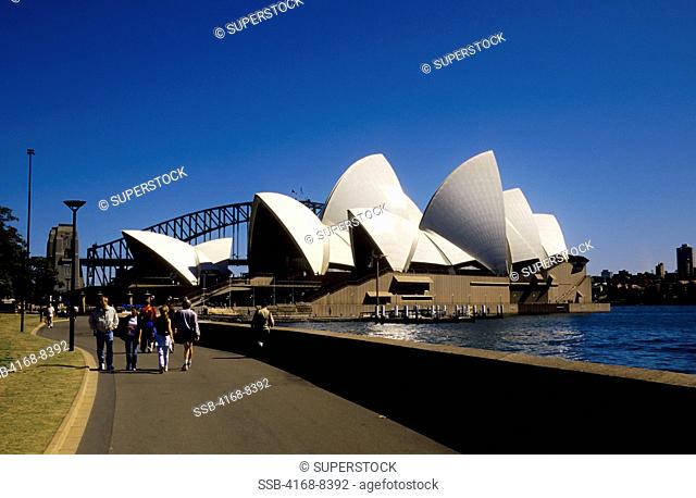 Australia, Sydney, People walking on promenade, Opera House with Harbor Bridge in background