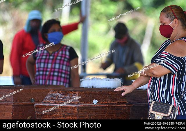 17 January 2014, Brazil, Manaus: A woman with a face mask is crying at the coffin of a relative in the cemetery. In view of the increasing number of corona...