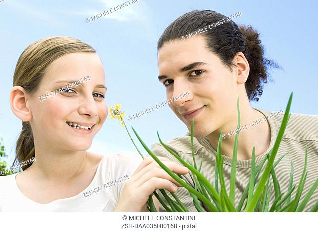 Young man and preteen girl with flowering aloe plant, smiling at camera