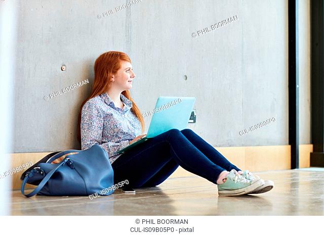 Young female student sitting on floor with laptop at higher education college