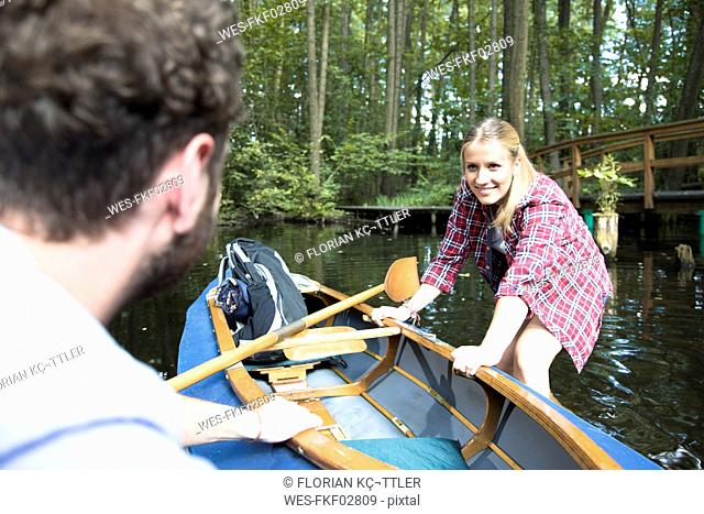 Happy young couple entering canoe in a forest brook