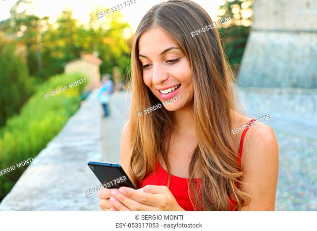 Happy beautiful woman send messages with application on the mobile phone outdoor