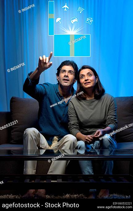 Indian middle age married couple dreaming about future while sitting on sofa