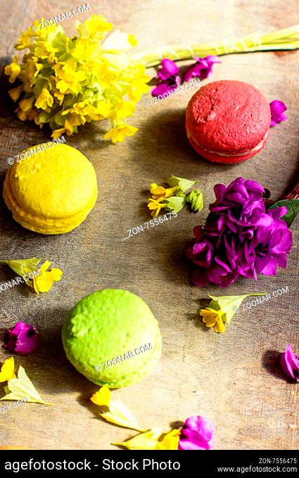 Colorful macaroons and first spring flowers on old wooden background
