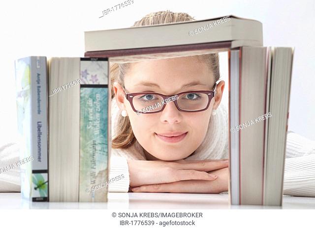 Young woman with glasses looking through a stack of books
