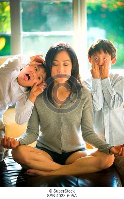 Mid adult woman being hassled by her children while doing yoga