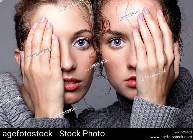 Two young women in gray sweaters on grey studio background. Beautiful girls stretching hands forward in embrace. Female friendship concept