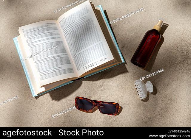 book, sunglasses and sunscreen on beach sand