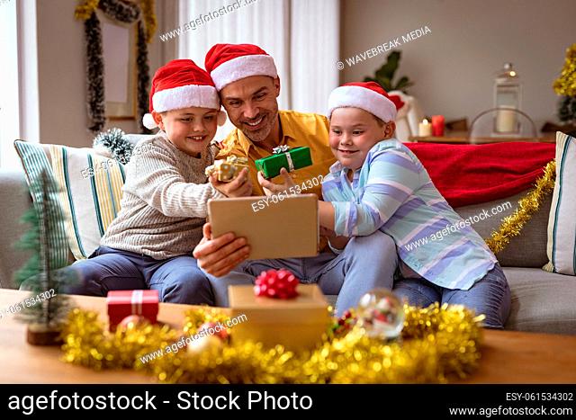 Caucasian father and two sons showing gifts during video call on digital tablet during christmas