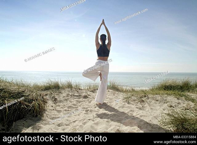 Young woman practices yoga on the beach