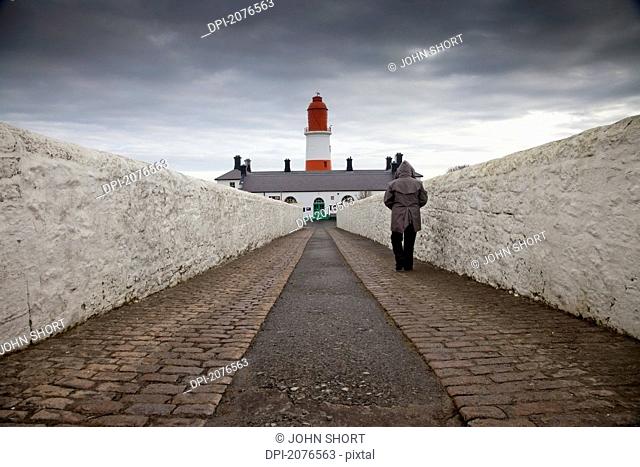 Person walking on a paved walkway towards a lighthouse, south shields tyne and wear england