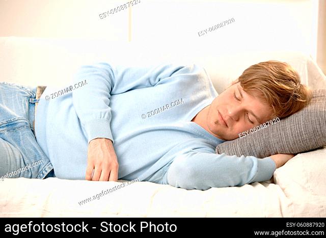 Tired young man sleeping on couch, taking afternoon nap