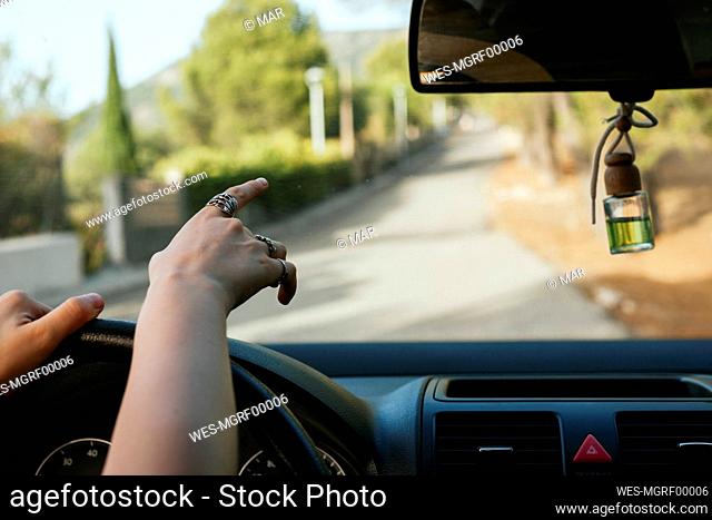 Hand of young woman pointing at road from car interior