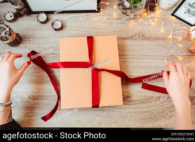 Woman's hands wrapping handmade present in paper with red ribbon