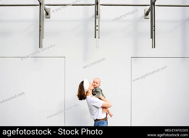 Mother kissing baby boy in front of wall