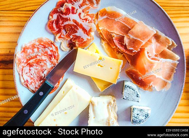 Plate with a variety of Italian cheese and charcuterie, on a wooden table