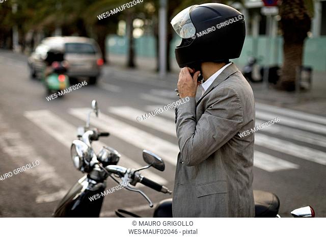 Businessman next to motorscooter putting on helmet