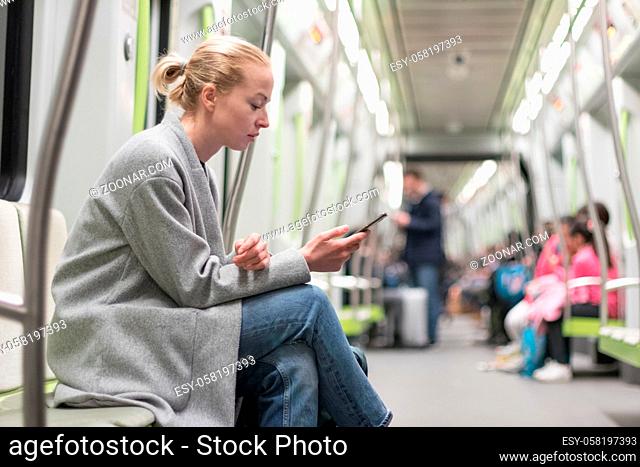 Portrait of lovely girl typing message on mobile phone in almost empty public subway train. Staying at home and social distancing recomented due to corona virus...