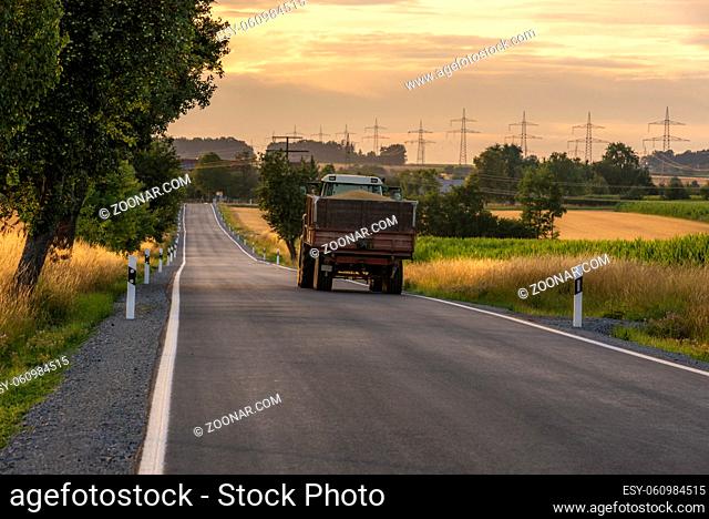 Harvest day image with a truck loaded with grains going on a long country road, at sunset, near Schwabisch Hall town, Germany