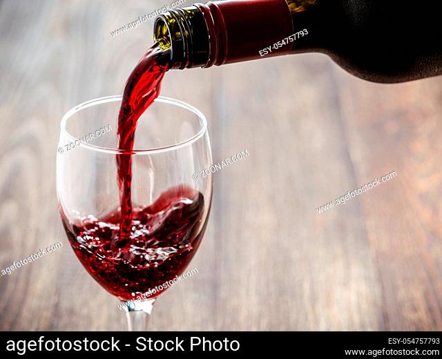 Closeup of red wine pouring in glass. Copy space. Sunflare effect